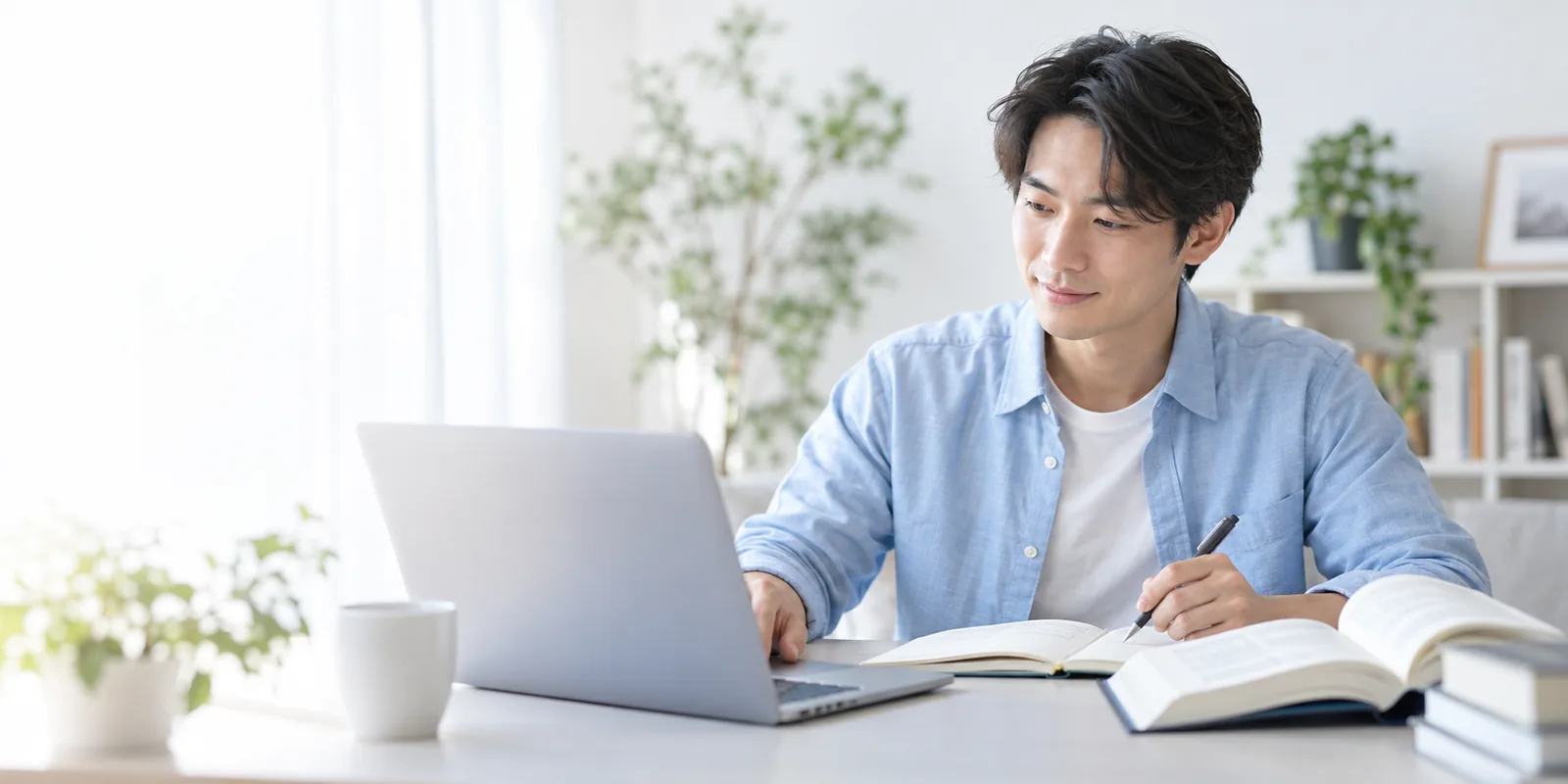 明るい学習環境で、ノートとパソコンを使って学ぶ成人学習者